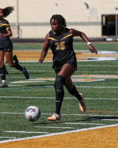 Soccer player in black uniform dribbling the ball on a field during a match.
