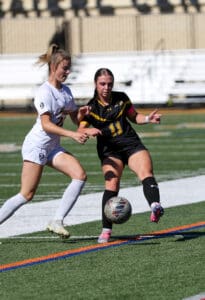 Two female soccer players competing for the ball on a sunny field.