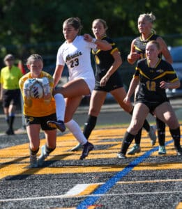 Girls' soccer game action with a goalie catching the ball and players in black and white jerseys in the field.