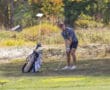 Golfer preparing to swing on a sunny golf course, with a golf bag nearby.