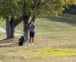 Golfer using rangefinder on a sunny course, surrounded by trees, with golf bag nearby.