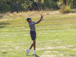 Young golfer swinging club on sunny green golf course.