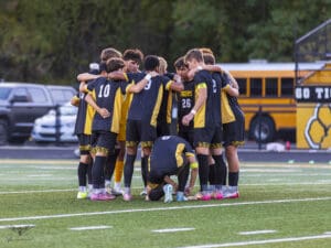 Soccer team huddling before a match on the field with Go Tigers bus in the background.