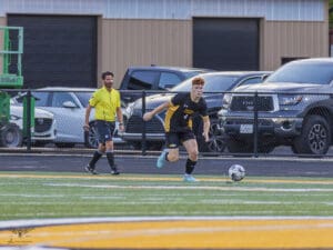 Soccer player dribbling the ball on a field as referee runs alongside.