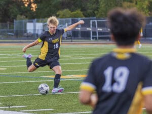 Soccer player in black and yellow uniform kicking a ball during a game on a green field.