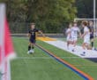 Soccer player in black uniform dribbles the ball along the sideline, pursued by opponents in white uniforms.