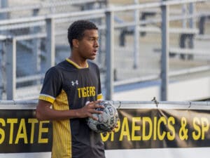 Soccer player prepares to throw in the ball during a game, wearing a black and yellow Tigers jersey.