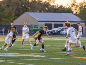 Youth soccer match action on the field with players in black and white uniforms competing for the ball.