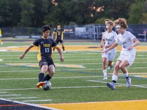 Soccer players competing on field, one in black Tigers jersey controlling ball, two in white Butler jerseys approaching.