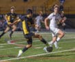 High school soccer match with players in action on the field, wearing contrasting black and white uniforms.