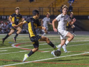 High school soccer match with players in action on the field, wearing contrasting black and white uniforms.