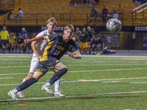 Soccer players competing for the ball during a match on a vibrant green field, with a focused crowd in the background.