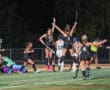 Field hockey team celebrates scoring a goal under stadium lights at night.