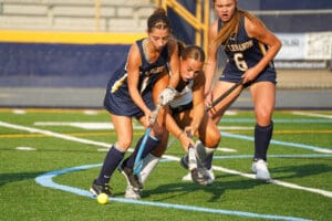Field hockey players competing for the ball on a sunny day during a match.
