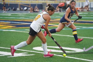 Two field hockey players compete for the ball on a green turf field during a match.