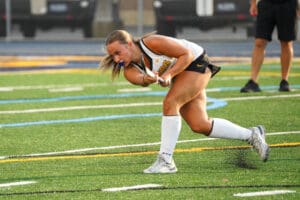 Field hockey player in action swinging stick on a turf field, wearing white socks and black shorts.