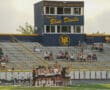 High school field hockey game at Mt. Lebanon Stadium, Blue Devils, with players huddled and spectators in stands.