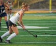 Young female field hockey player in action on a turf field, focused and ready to pass the ball.