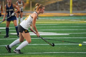 Young female field hockey player in action on a turf field, focused and ready to pass the ball.