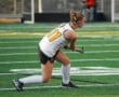 Field hockey player in action, poised with stick on green turf field, wearing jersey number 11.