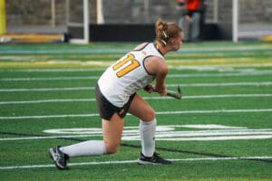 Field hockey player in action, poised with stick on green turf field, wearing jersey number 11.