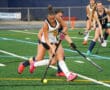 Field hockey players in action, competing for the ball on a green turf field.