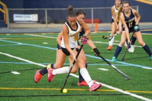 Field hockey players in action, competing for the ball on a green turf field.