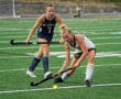 Two field hockey players competing for the ball during a match on a green field.