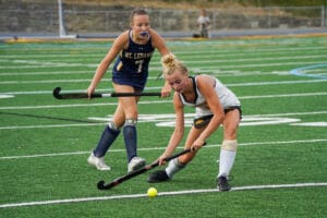 Two field hockey players competing for the ball during a match on a green field.
