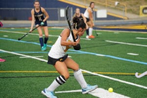 Field hockey player preparing to hit the ball during a competitive match on a grass field.