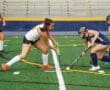 Girls playing field hockey on a turf field, competing intensely for the ball.