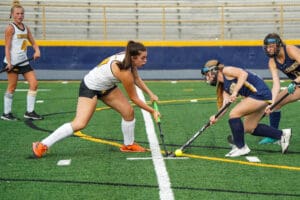 Girls playing field hockey on a turf field, competing intensely for the ball.