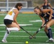 Two female field hockey players competing intensely on a green field, focusing on the yellow ball.
