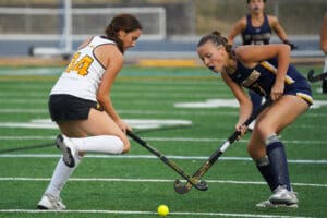 Two female field hockey players competing intensely on a green field, focusing on the yellow ball.