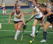 Field hockey game action with players in pursuit of the ball on a green turf field.