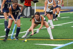Field hockey players competing intensely on a vibrant green turf, sticks poised for action over the ball.