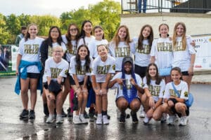 Group of girls in Own the Field shirts posing outdoors, smiling and cheerful.