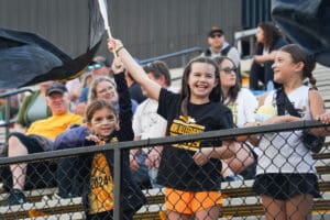 Children enjoying a sports event, waving a flag with excitement in the stadium stands.
