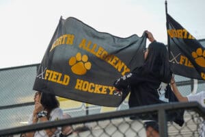 Fans waving North Allegheny field hockey flags at a game, promoting school spirit.