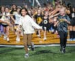 Children excitedly run through a group high-five line at a sports event on a turf field.
