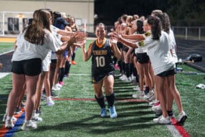 Field hockey player high-fives teammates on the field, wearing a Tigers jersey, surrounded by cheering team members.