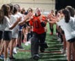 Field hockey goalie celebrates with teammates in a high-five tunnel on the field.