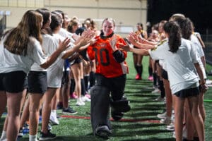 Field hockey goalie celebrates with teammates in a high-five tunnel on the field.