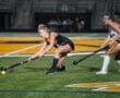 Two female field hockey players in action on a turf field during a competitive night match.