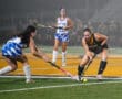 Field hockey players in action during a match at night, competing intensely for the ball on the field.