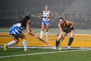 Field hockey players in action during a match at night, competing intensely for the ball on the field.