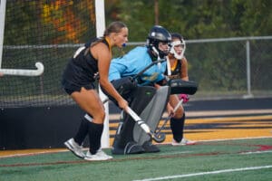 Field hockey players ready in defense during a match, focused and prepared near the goal.