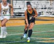 Field hockey players compete on turf during a match, focusing on the ball.