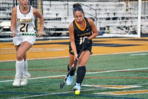 Field hockey players compete on turf during a match, focusing on the ball.