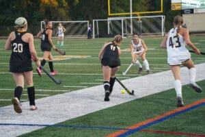 Field hockey players in action on a green turf field during a competitive game.